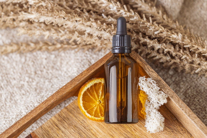 Natural face serum bottle with dried botanicals and an orange slice on a warm wooden tray