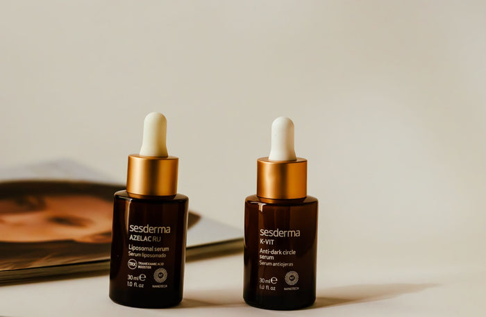 Two amber glass dropper serum bottles arranged on a warm neutral surface