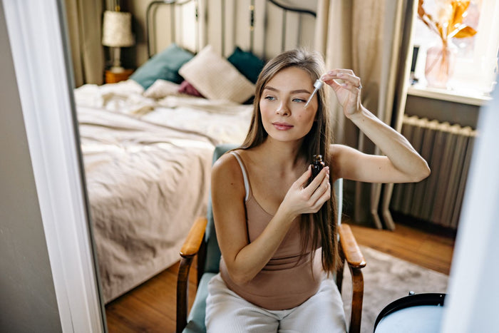 Woman applying a night serum with a dropper in a warm, cozy evening setting