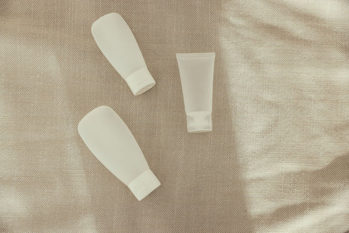 Minimalist unbranded skincare bottles on a warm neutral fabric