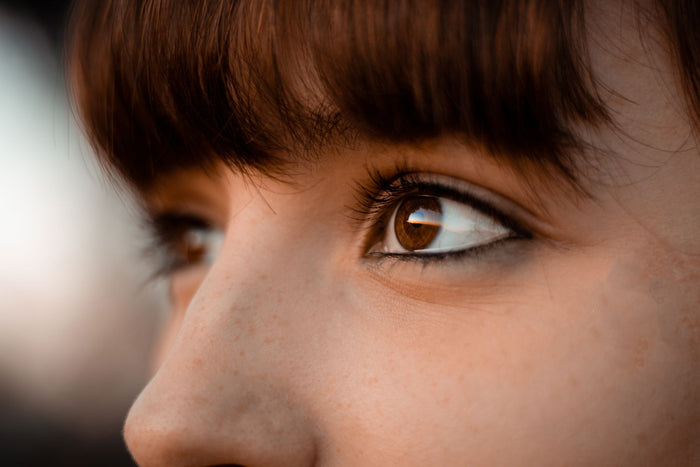 Close-up of a woman's under-eye area and brown eye in natural light