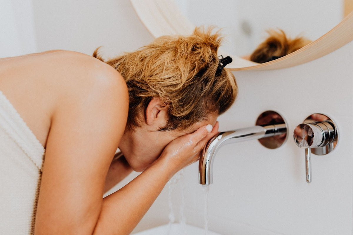 Woman washing her face at a bathroom sink during her morning routine