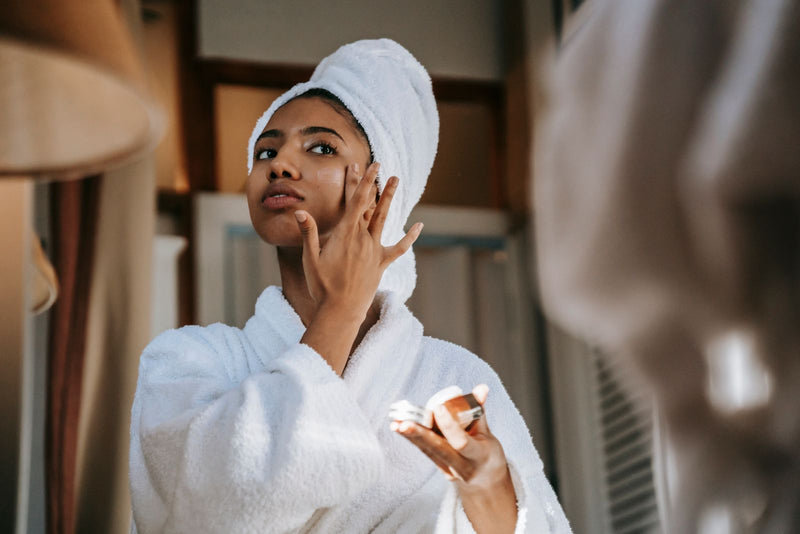 Woman applying cream to her face in front of a mirror