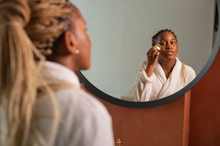 Young woman applying a skincare serum at a mirror in warm natural light