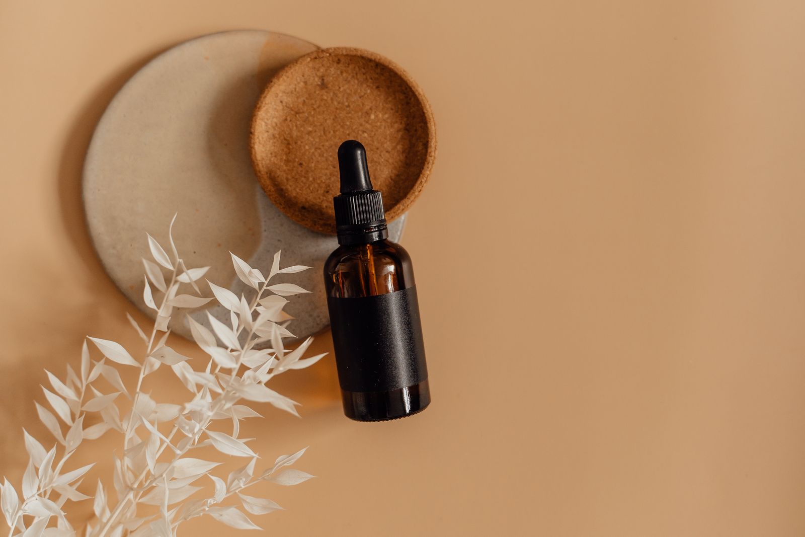 Minimalist skincare serum dropper bottle with dried botanicals on a warm neutral background