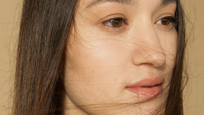Close-up of a woman with clear, healthy brown skin and natural texture in soft light