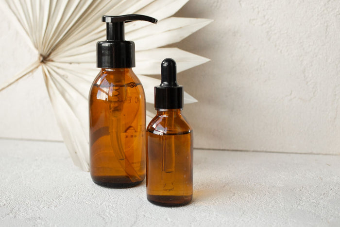 Two amber dropper serum bottles on a minimalist warm surface